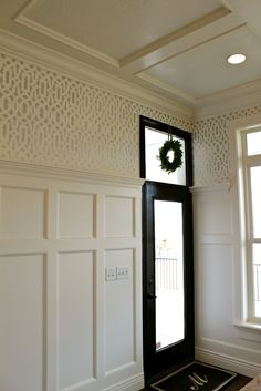 a black door with a wreath on it in front of a white wall and windows