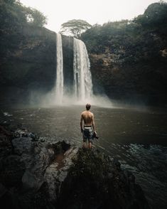 a man standing in front of a waterfall with his back turned to the camera,