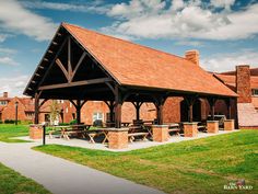 an outdoor pavilion with picnic tables and benches on the grass in front of brick buildings