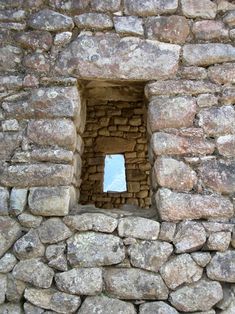 a stone wall with a small window in the center and sky reflected in the hole