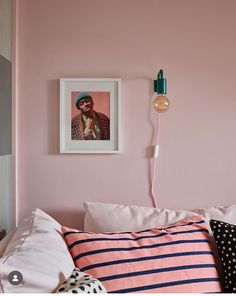 a bedroom with pink walls and black and white striped pillows, a framed photograph on the wall