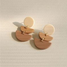 two tone drop earrings with gold accents on a white background, one is brown and the other is beige