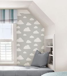 a bed sitting under a window next to a wall mounted book shelf in a bedroom