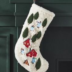 a white christmas stocking hanging from a hook on a green painted wall with houses and trees