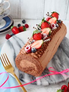 a piece of chocolate cake on a plate with strawberries and blueberries around it