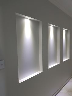 three windows with light coming through them in a room that has white walls and tile flooring