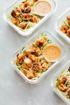 four plastic containers filled with food on top of a white countertop next to dipping sauces