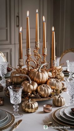 a centerpiece with gold pumpkins and candles on top of a dining room table