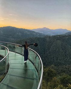 a woman standing on the edge of a glass walkway with mountains in the back ground