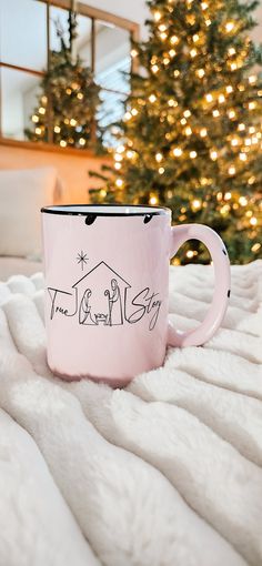 a pink coffee mug sitting on top of a white blanket next to a christmas tree