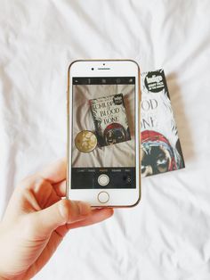 a person holding an iphone in front of a book on a white bed with sheets