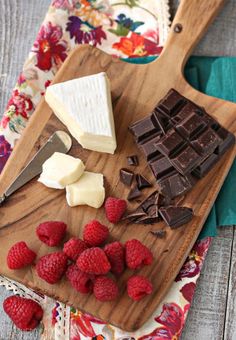 chocolate, raspberries and butter on a cutting board next to a flowered cloth