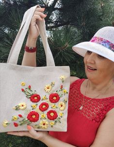 a woman is holding a bag with flowers on it and wearing a white sunhat