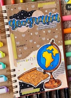 an open notebook with the words geographia written on it next to crayons