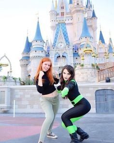 two women in black and green outfits posing for a photo near a castle at disney world