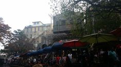 an outdoor market with people walking around and umbrellas on the side of the street