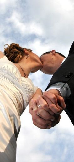 a bride and groom are kissing in front of the sky