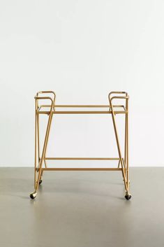 a gold bar cart with two handles and wheels on the bottom, in front of a white wall