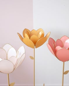 three different colored flowers on sticks in front of a white wall and pink flooring