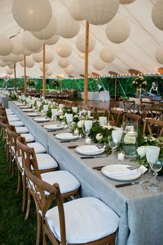 a long table is set with white plates and place settings for an outdoor wedding reception