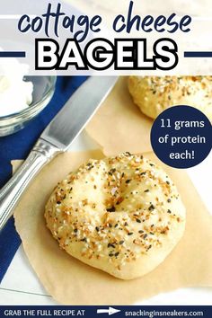 two bagels sitting on top of parchment paper next to a knife and bowl of cream cheese