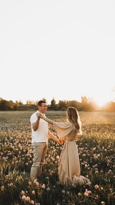 a man and woman standing in a field holding each other's hands as the sun sets behind them