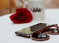 a cell phone sitting on top of a white table next to a cup and red rose