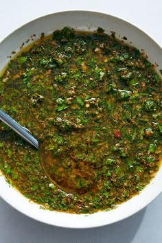 a white bowl filled with green soup on top of a table next to a spoon