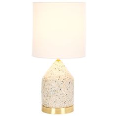 a white and gold table lamp with a white linen shade on the base, against a white background