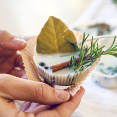 a person holding a cupcake with leaves and spices on it in front of other food items