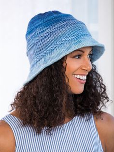 a woman with curly hair wearing a blue knitted hat and smiling at the camera