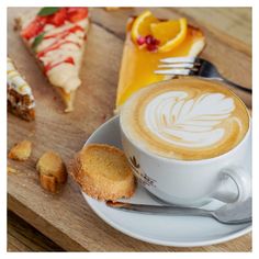 a cappuccino on a saucer next to pastries and orange slices