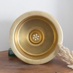 a golden sink sitting on top of a wooden table next to a roped plant