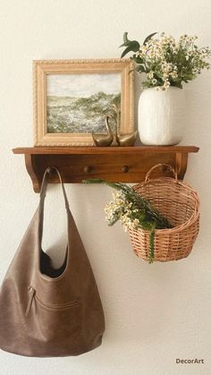 a brown purse hanging on a wall next to a basket with flowers and a painting