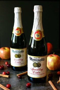 two bottles of wine sitting on top of a table next to apples and cinnamon sticks