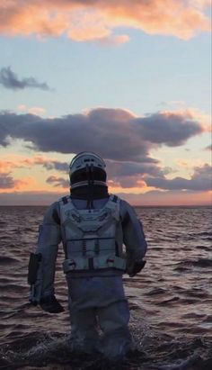 an astronaut is standing in the water looking out at the sun set over the ocean