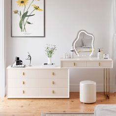 a white dresser sitting next to a mirror on top of a wooden floor in a room