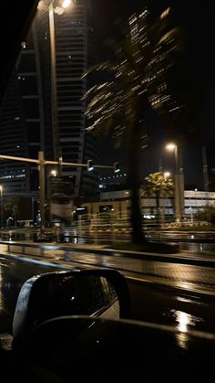 a city street at night with cars driving on the road and tall buildings in the background