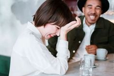 two people sitting at a table with cups and saucers in front of them smiling