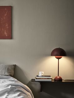 a bed with white sheets and a red lamp on top of it next to a painting