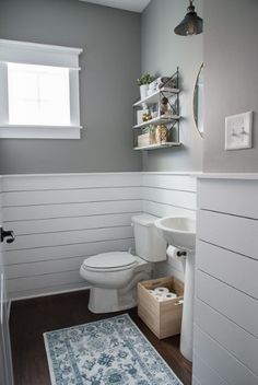 a white toilet sitting next to a sink in a bathroom under a window on top of a wooden floor