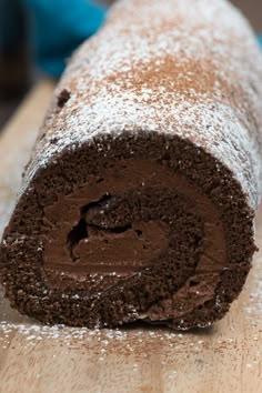 a chocolate cake roll is on a wooden surface with powdered sugar around the edges