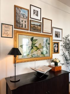 a wall with many framed pictures on it and a lamp in front of the table