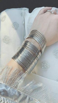 a woman's arm is covered with silver bracelets and rings, while wearing a white dress