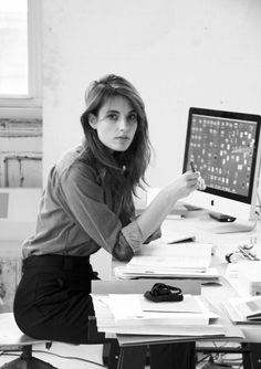 a woman sitting at a desk writing on a piece of paper with a computer in the background