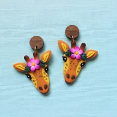 two giraffes with flowers on their heads are hanging from ear hooks, against a blue background