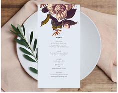 a white plate topped with a menu next to a green leafy plant on top of a wooden table