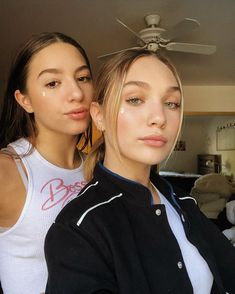 two young women standing next to each other in front of a ceiling fan and looking at the camera