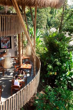 people are sitting at wooden tables under thatched umbrellas in the tropical garden area