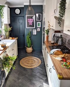 a kitchen with white cabinets and wooden counter tops next to a black door that has plants on it